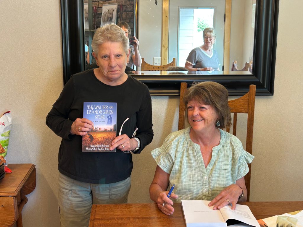 Author Sherry Gillen sitting at a table smiling alongside a guest holding a copy of The Walter and Eleanor Gillen Story